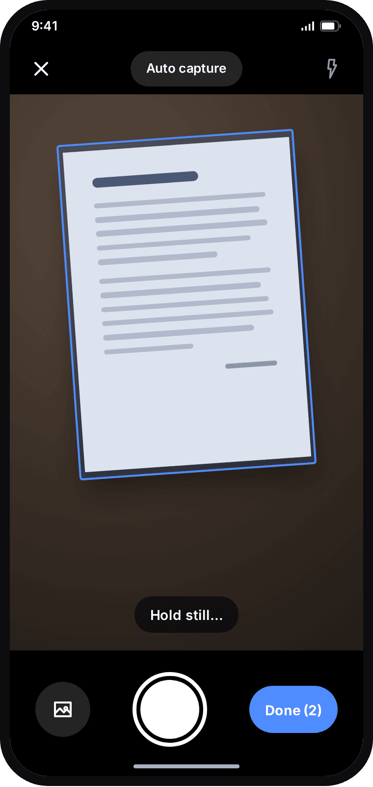 Keepscan camera outlining a page on a desk in blue, with the hint Hold still